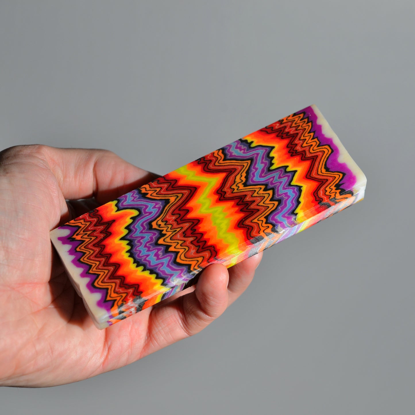 Bright multicolor composite knife handle block with layered lava pattern held in hand #01