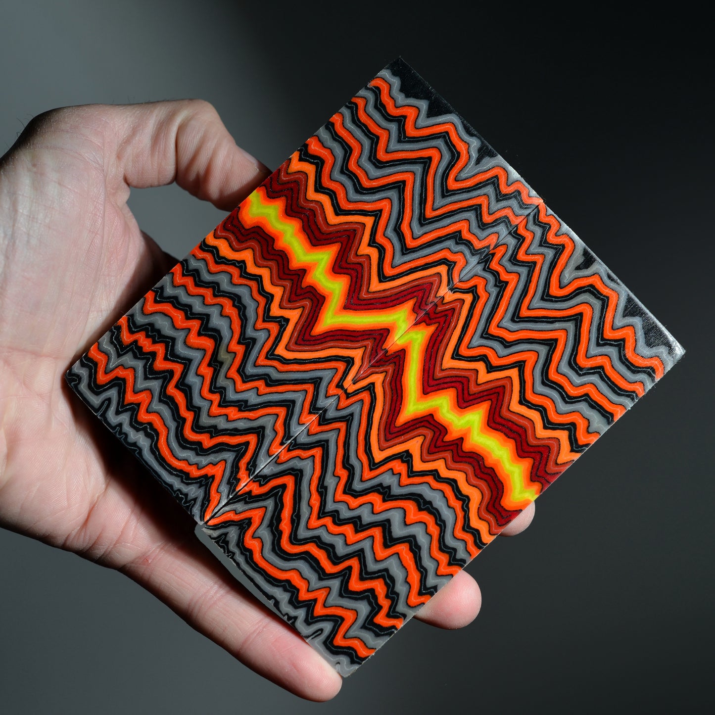 A book-matched pair of premium custom micarta knife scales featuring a high-contrast orange, charcoal, and neon yellow lightning zigzag pattern with a wavy texture.