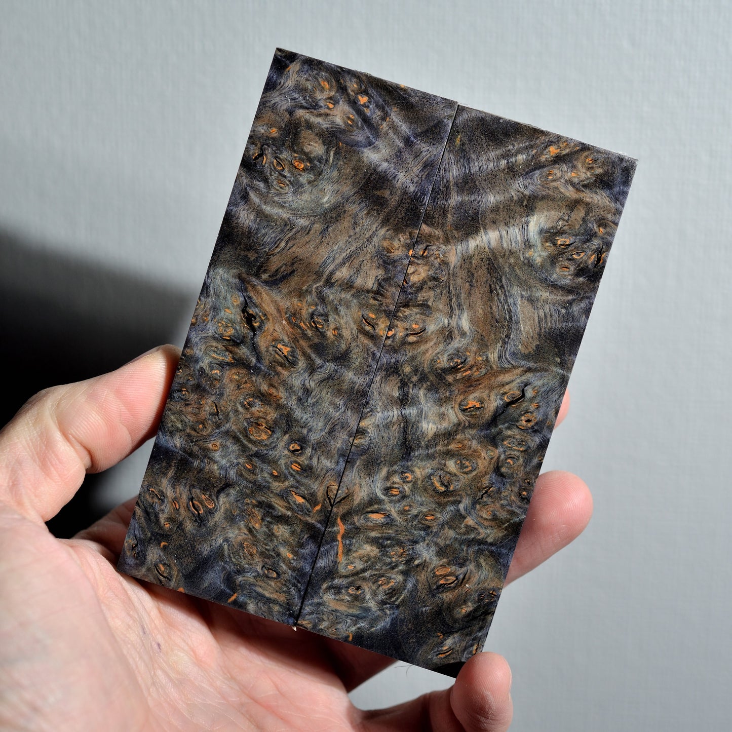 Bookmatched stabilized Alder Burl knife scales with a unique stormy grey and blue tint, featuring fine orange burl eyes and marble-like texture.