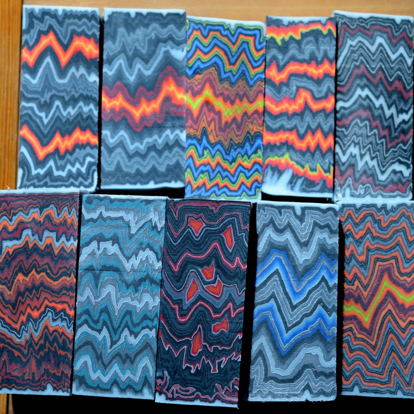 Wholesale set of 10 custom composite knife handle blocks featuring assorted high-contrast wave and zigzag patterns in orange, blue, grey, and multi-color themes.