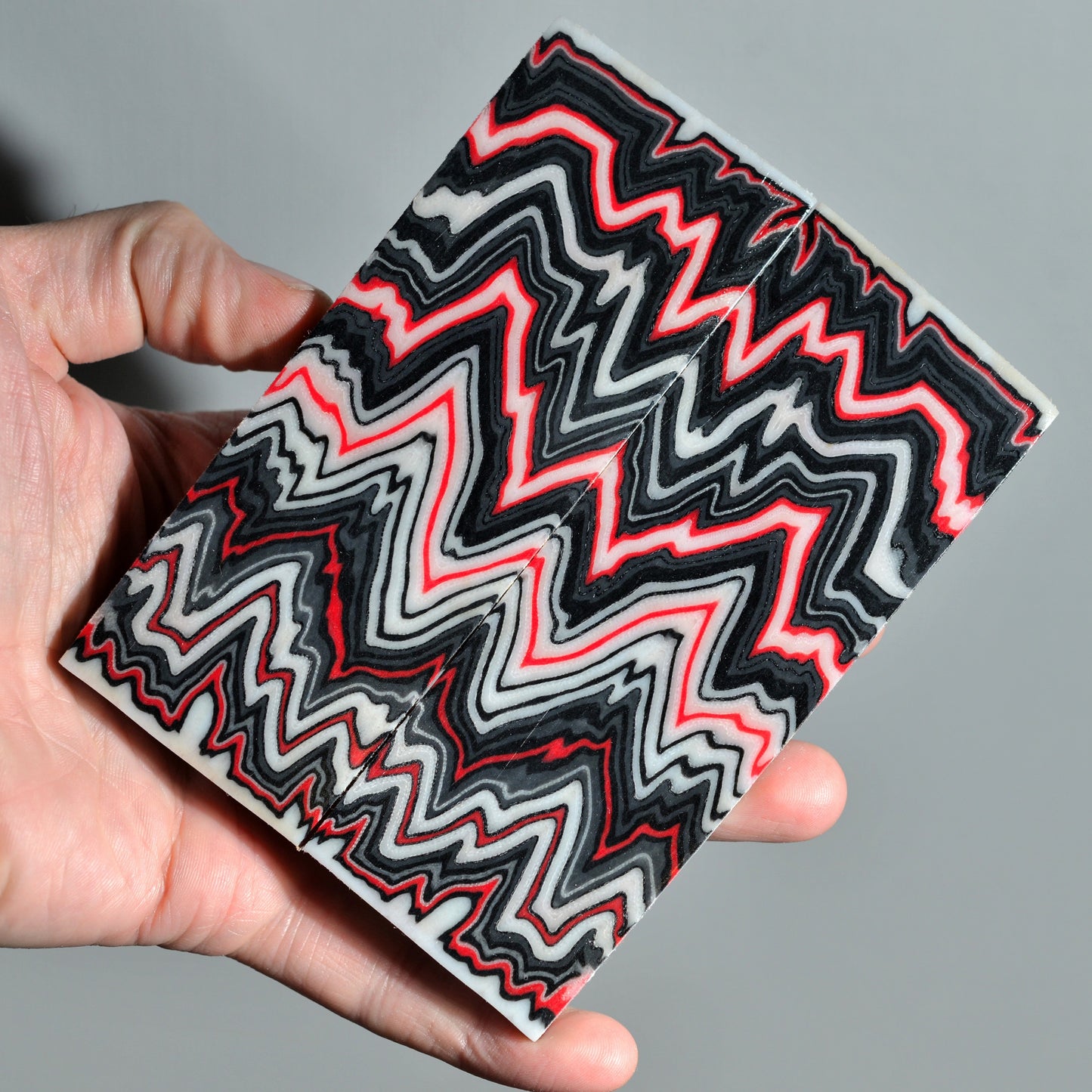Custom micarta block with bold zigzag design in black, white and red colors.