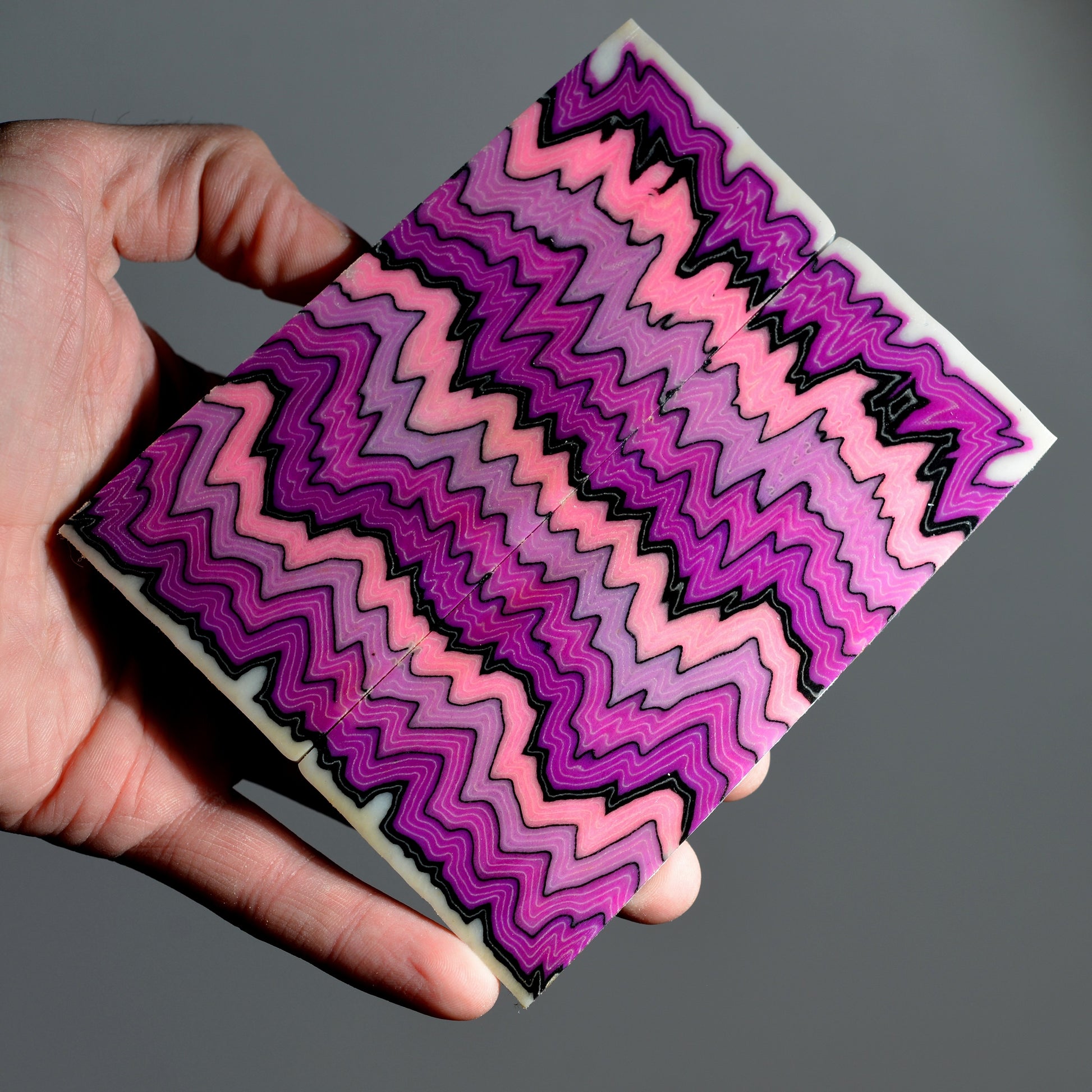 A pair of custom micarta knife scales with a symmetrical zigzag pattern in vibrant shades of pink, magenta, purple, and black.