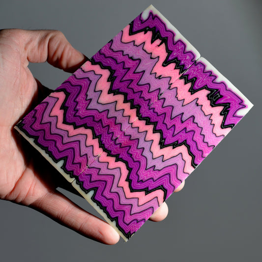 A pair of custom micarta knife scales with a symmetrical zigzag pattern in vibrant shades of pink, magenta, purple, and black.
