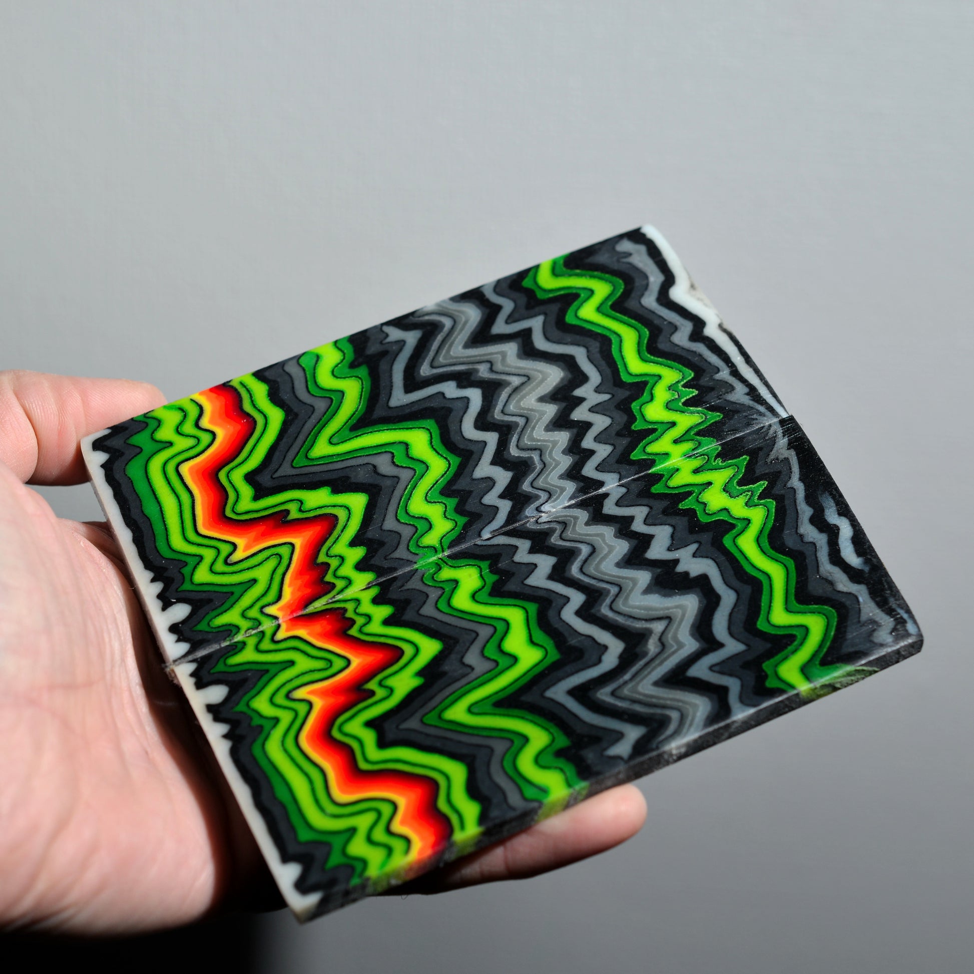 Handmade micarta block with neon green, black, gray and red zigzag pattern for knife handles.