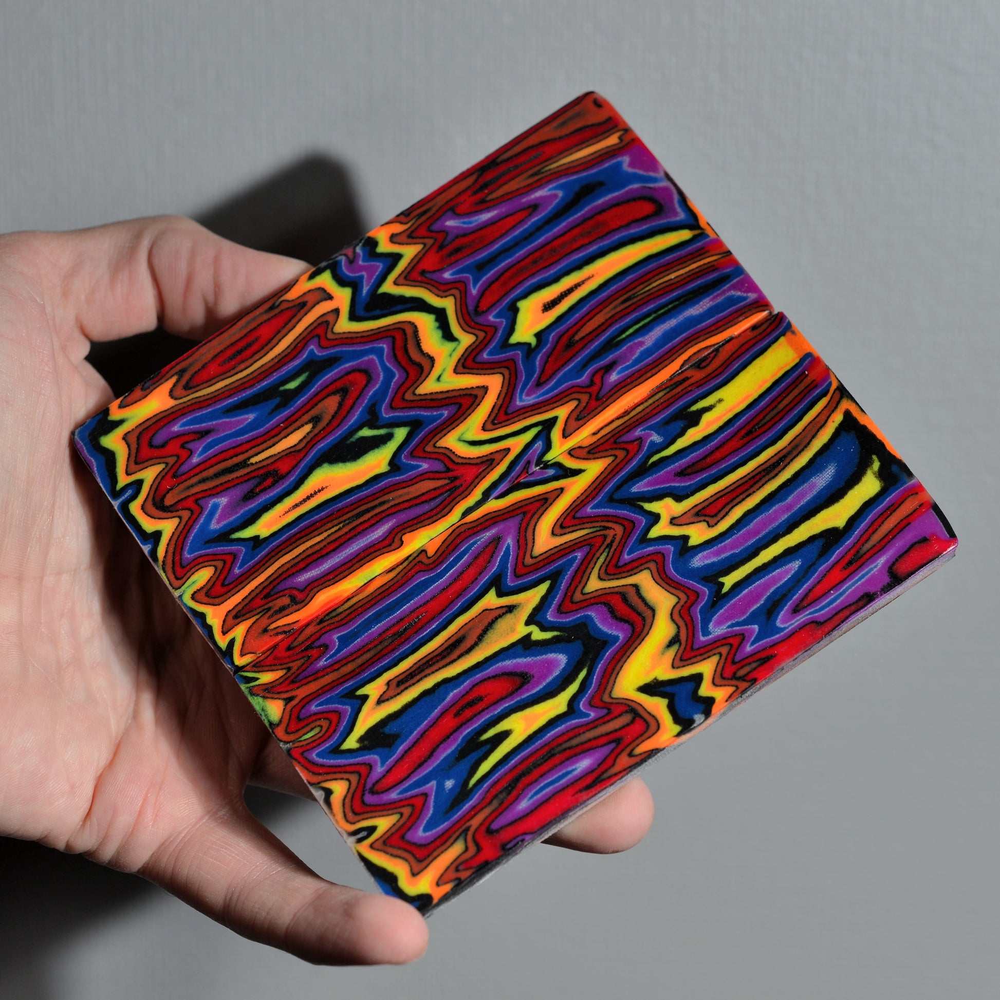 Large artisan canvas composite block in "Neon Nebula" colors held in hand to show the high-contrast fabric laminate layers for knifemaking.