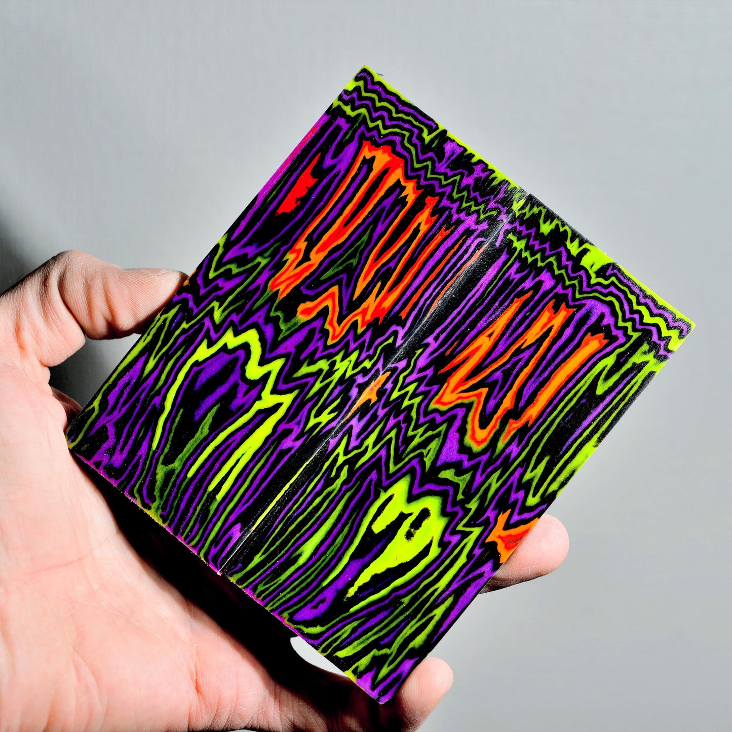 High-contrast bookmatched micarta knife scales with a vibrant neon wave pattern in purple, electric green, and bright orange.