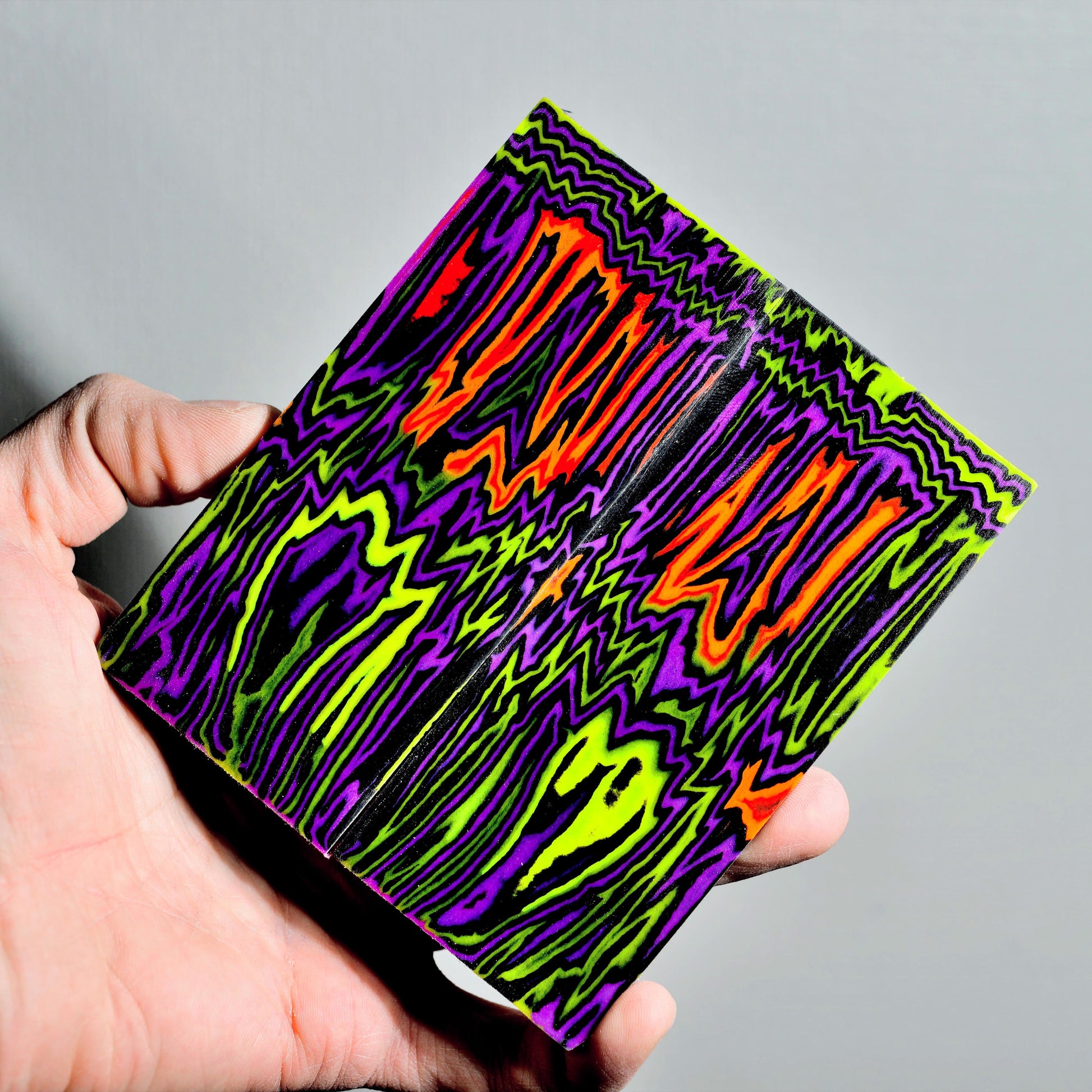 High-contrast bookmatched micarta knife scales with a vibrant neon wave pattern in purple, electric green, and bright orange.