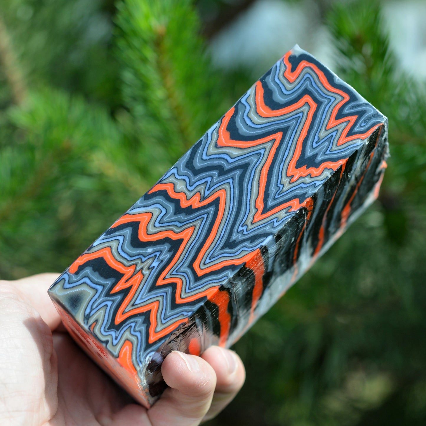 A solid block of premium micarta with a high-contrast 'Lava Flow' zigzag pattern in fiery orange, deep black, and grey for custom knife handle carving.