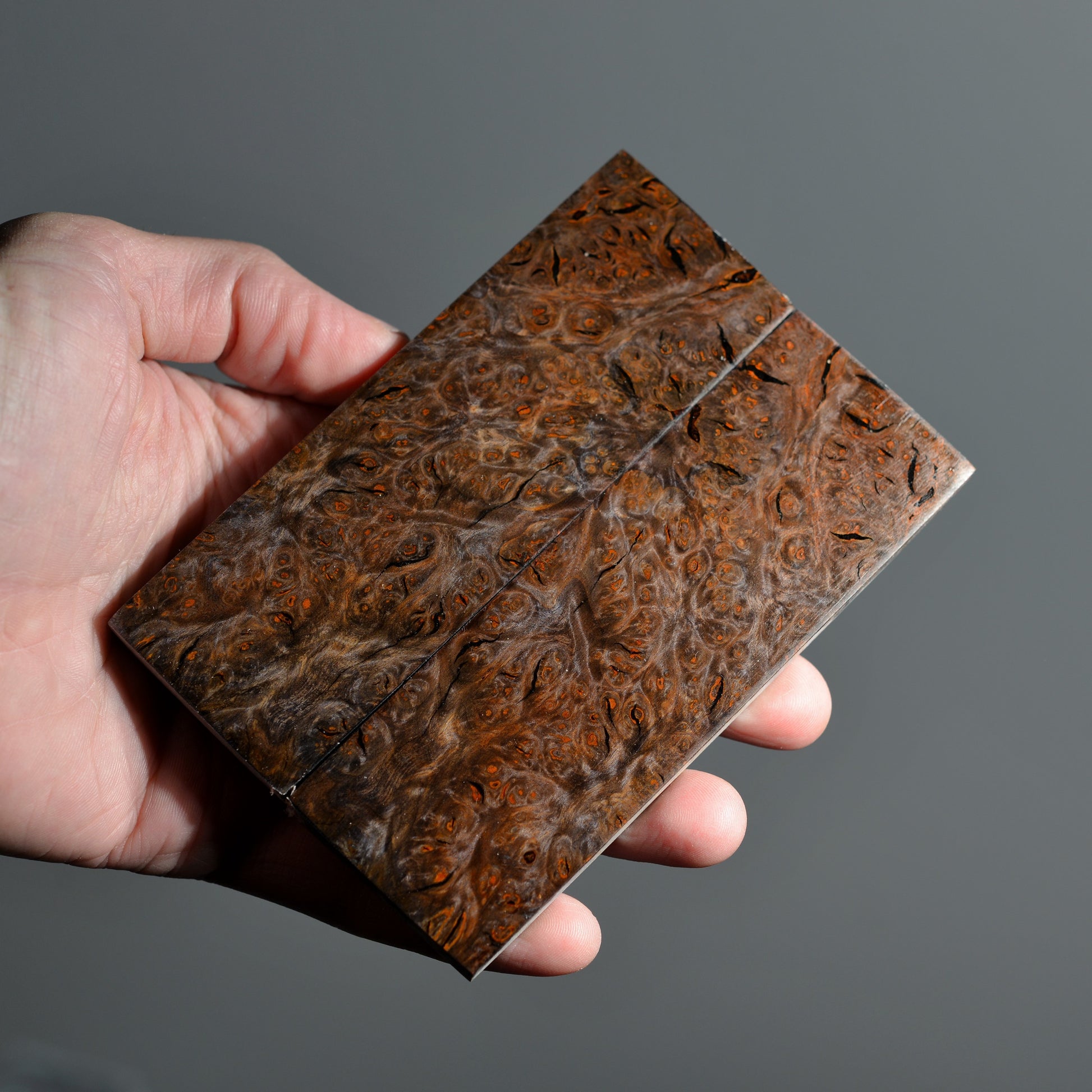 Stabilized alder burl wood handle scales with rich burl figure held in hand.