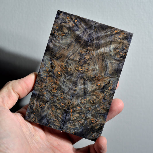 Bookmatched stabilized Alder Burl knife scales with a unique stormy grey and blue tint, featuring fine orange burl eyes and marble-like texture.
